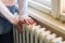 Mädchen im Wollpullover legt Hände auf einen älteren Heizkörper. (Bild: ©Zvone/Shutterstock.com)